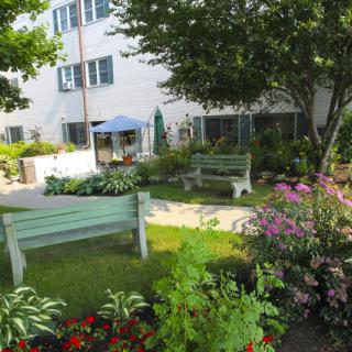A peaceful garden area with benches, colorful flower beds, and a nearby building.