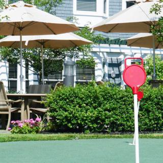A shuffleboard court in a garden setting with patio umbrellas and seating.