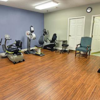 A small exercise room with various fitness equipment and wooden flooring.
