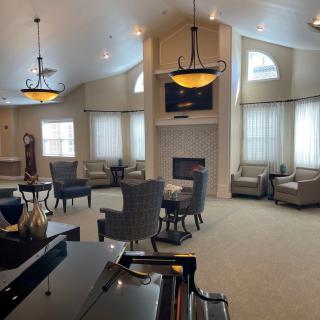 A spacious living room with elegant furniture, a fireplace, and a grand piano under stylish chandeliers.