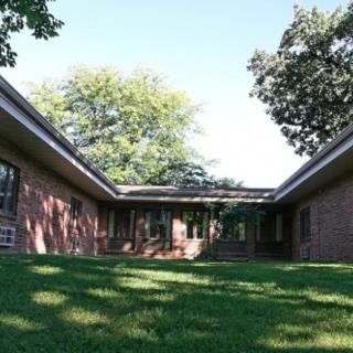 A brick residential house with a spacious yard surrounded by trees.
