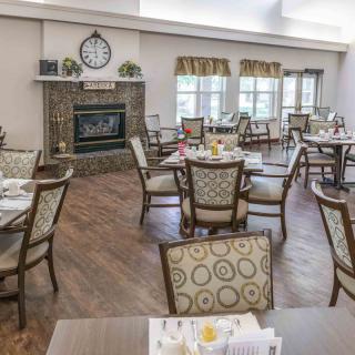 A well-arranged dining area with wooden flooring, featuring elegant chairs and tables, a fireplace, and large windows.