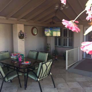 A cozy outdoor patio with seating, a television, and vibrant flowers.