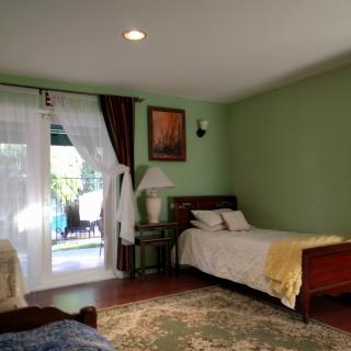 A cozy bedroom with a single bed and green walls, featuring a window with curtains, a nightstand, and a lamp.