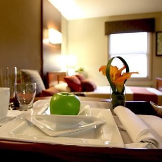 A cozy hotel room with a tray featuring an apple, glassware, and flowers on the side table.