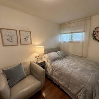 A cozy bedroom featuring a neatly made bed, an armchair, a table lamp, and decorative artwork on the walls.
