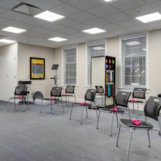 An empty, modern waiting room with chairs arranged in rows and large windows providing natural light.
