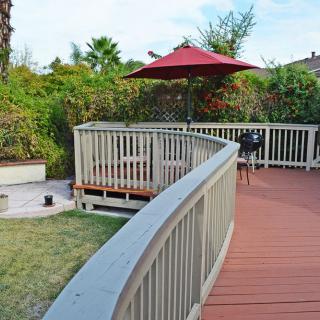 A cozy outdoor deck with a red umbrella and surrounding garden.