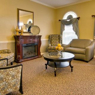 A cozy living room with a classic design, featuring a sofa, two armchairs, a central coffee table, and an ornate fireplace.
