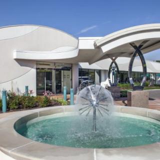 A modern building with a unique curved roof and a decorative fountain in the foreground.