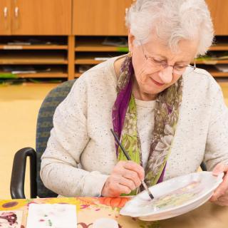 An elderly woman engaging in a painting activity indoors.