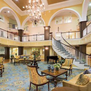 A beautifully designed hotel lobby featuring an elegant chandelier, a grand staircase, and comfortable seating areas.