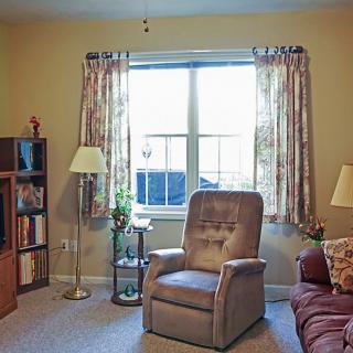 A cozy living room with a recliner, bookshelf, and window with curtains.
