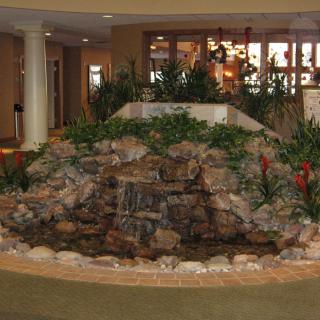 An indoor waterfall with rocks and lush greenery in a well-lit interior setting.