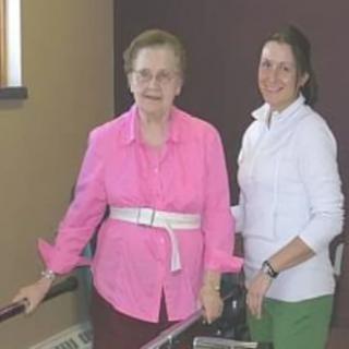 Two women standing indoors, one using a walker.