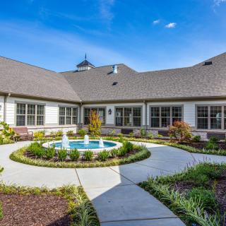 A beautifully landscaped courtyard with a central fountain surrounded by pathways and a building in the background.