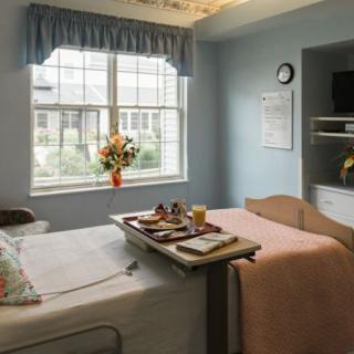 A hospital room with a bed, tray table, and flowers by the window.