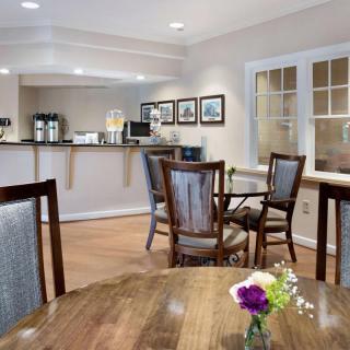 A cozy dining area with wooden tables, chairs, a coffee station, and decorative flowers.