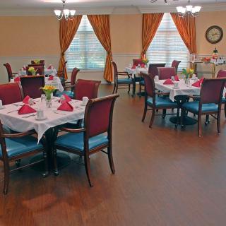 A cozy dining area with elegantly set tables and chairs, featuring warm curtains and natural lighting.