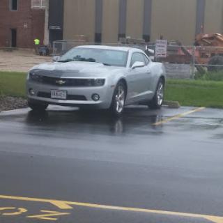A silver Chevrolet Camaro parked in a rainy parking lot.