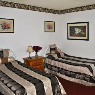A cozy bedroom featuring two twin beds with matching bedspreads, complemented by framed artwork and a wooden nightstand.