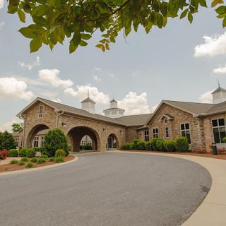 A large stone building with a circular driveway and neatly maintained landscaping beneath a cloudy sky.