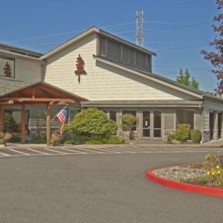 A building with an entrance, featuring an American flag and surrounding landscaping on a sunny day.