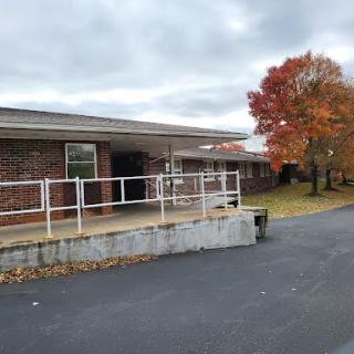 An exterior view of a building surrounded by autumn foliage and a cloudy sky.