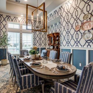 A stylish dining room with patterned wallpaper and striped chairs, featuring a beautifully set table and ample natural light.