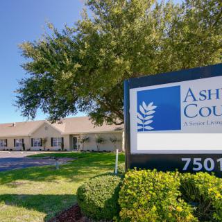 A sign in front of a building with trees and grass on a clear day.