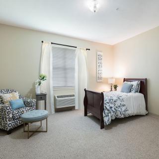A cozy bedroom with a bed, armchair, and window creating a serene atmosphere.