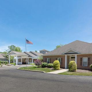 A building with a flagpole flying the American flag, featuring a landscaped entrance and clear blue sky.