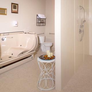 A modern bathroom featuring a jacuzzi tub, toilet, and walk-in shower with decorative candles on a side table.