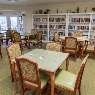 A cozy reading room with tables and chairs surrounded by bookshelves.
