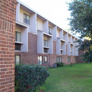 A brick apartment building with multiple floors and a landscaped lawn.