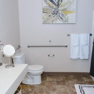 A clean and modern bathroom with a toilet, sink, mirror, towels, and artwork on the wall.
