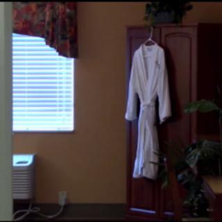 A white robe hanging on a cabinet next to a window with blinds and floral curtains.