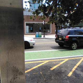 A view of a city street featuring parked cars and a green bike lane.