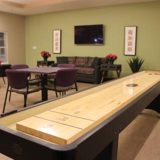 A cozy game room featuring a shuffleboard table, comfortable seating, and a mounted TV on the wall.
