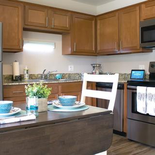 A modern kitchen with wood cabinets, stainless steel appliances, and a cozy dining area.