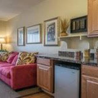 A cozy living space featuring a red couch and a kitchenette with wooden cabinets and decorative wall art.