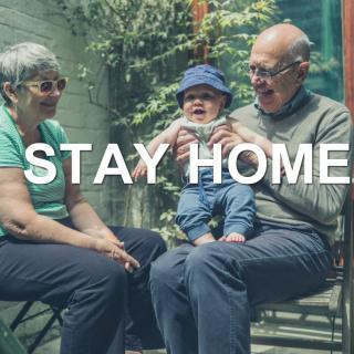 A family with grandparents and a child sitting outside, emphasizing the message 'Stay Home'.
