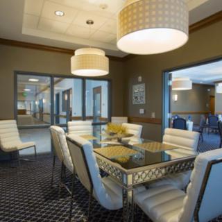 A modern dining room with a glass table, upholstered chairs, and stylish lighting.
