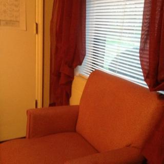 A cozy room corner featuring an orange armchair next to a window with blinds and curtains.
