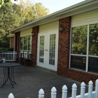 A serene patio area with brick walls and large glass doors, framed by a white picket fence.