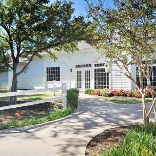 A charming white house with a winding pathway, surrounded by trees and well-kept shrubbery on a sunny day.