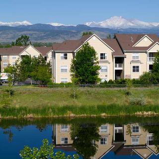 Apartment buildings reflected in a lake with mountains in the background.