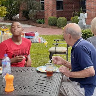 A young boy and an elderly man enjoying a meal together in an outdoor setting.