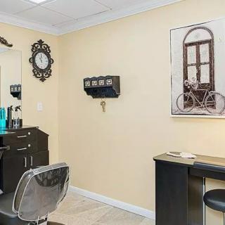A cozy hair salon interior featuring a styling chair, desk, mirror, and wall decor.