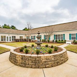A landscaped courtyard featuring a central fountain surrounded by a well-maintained garden and building.